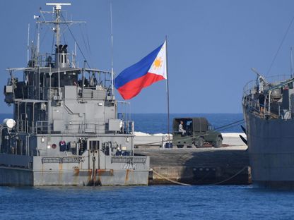 علم الفلبين بجوار سفن تابعة للبحرية راسية في جزيرة ثيتو ببحر الصين الجنوبي المتنازع عليه. 21 أبريل 2023 - AFP