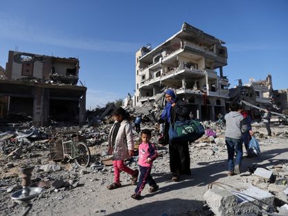 أسرة فلسطينية نازحة تسير وسط منازل دمرتها غارة إسرائيلية في خان يونس جنوب قطاع غزة. 24 نوفمبر 2023 - Reuters