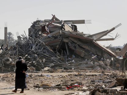 فلسطينيون يبحثون عن متعلقاتهم وسط أنقاض منزل قصفه الجيش الإسرائيلي في دير البلح بقطاع غزة. 20 يناير 2024 - AFP
