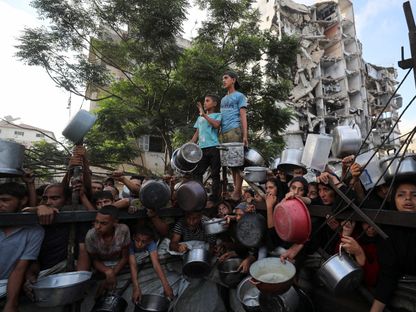 فلسطينيون ينتظرون الحصول على الطعام من مطبخ خيري، وسط أزمة جوع، بينما يقف مبنى مدمر في الخلفية، وذلك في مدينة غزة. 14 يوليو 2025. - Reuters