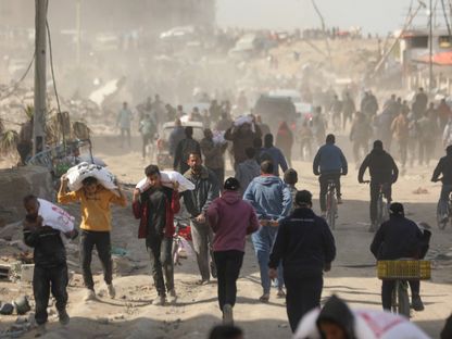 فلسطينيون يحملون بعض أجولة الدقيق فيما يسارع آخرون للحاق بشاحنة مساعدات إنسانية في مدينة غزة بينما يتواصل القصف الإسرائيلي المكثف على القطاع. 6 مارس 2024 - AFP