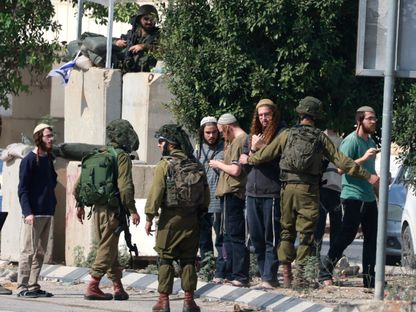 جنود إسرائيليون يقفون بجانب عدد من المستوطنين بعد اقتحامهم قرية دير شرف في الضفة الغربية. 2 نوفمبر 2023 - AFP