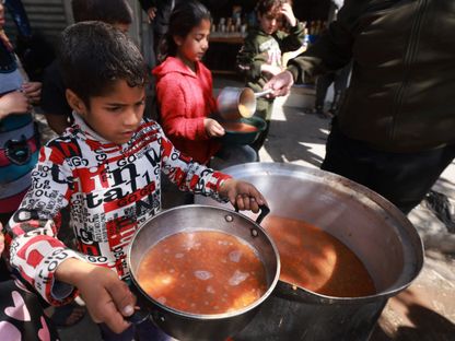 أطفال فلسطينيون خلال حصولهم على طعام في مخيم للنازحين جنوبي قطاع غزة بينما تستمر الغارات الإسرائيلية على القطاع. 5 مارس 2024 - AFP