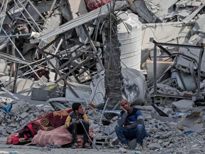 رجل فلسطيني وابنه يجلسون بجوار متعلقاتهم أمام حطام المنازل التي دمرتها الغارات الإسرائيلية على خان يونس جنوبي قطاع غزة. 14 مارس 2024 - AFP