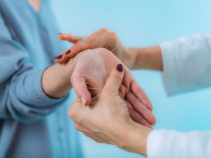 طبيبة تفحص يد مريض مسن يعاني من ألم في المعصم. 1 أبريل 2021 - AFP