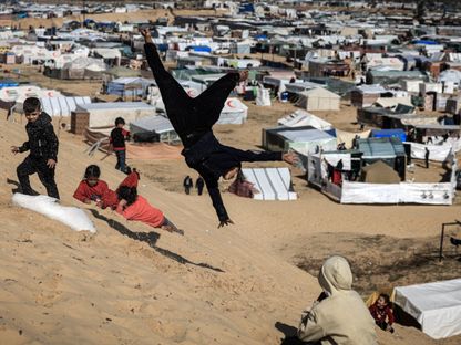 أطفال فلسطينيون بالقرب من مخيمات النازحين في رفح جنوبي قطاع غزة بينما يستمر القصف الإسرائيلي على كافة أنحاء القطاع. 14 يناير 2024 - AFP