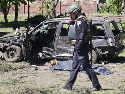 شرطي أوكراني يمر بجانب جثة ملقاة بالقرب من سيارة محترقة جراء استهدافها بقصف روسي في خاركوف. 1 مايو 2024 - AFP