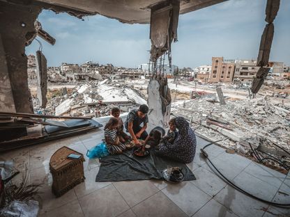 عائلة فلسطينية عائدة إلى خان يونس تتناول الطعام بين أنقاض منزلها الذي دمرته الغارات الإسرائيلية على غزة. 26 أبريل 2024 - AFP