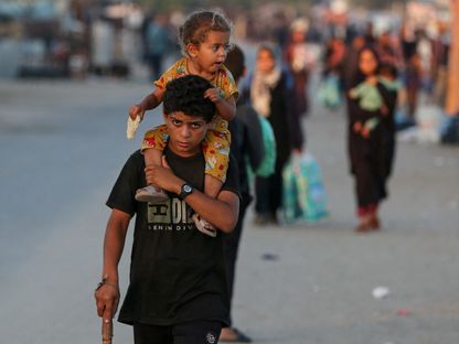 طفل فلسطيني يحمل طفلة أخرى خلال رحلة نزوح جديدة من رفح جنوبي قطاع غزة مع تصاعد الهجمات الإسرائيلية. 7 يونيو 2024 - Reuters