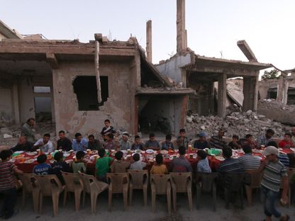سوريون ينتظرون الإفطار في رمضان بجانب أنقاض ومنازل مدمرة جراء غارات جوية في دوما، سوريا، 18 يونيو 2017. - AFP