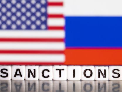 رسم توضيحي يتضمن العلمين الأميركي والروسي مع كلمة "عقوبات' بالإنجليزية. 01 مارس 2022 - REUTERS