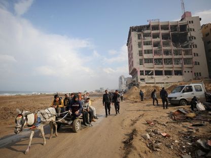 فلسطينيون يركبون عربة يجرها حمار عبر طريق شاطئي مدمر، وسط الحرب الإسرائيلية المستمرة في مدينة غزة. 19 فبراير 2024 - Reuters