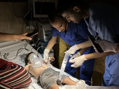 أطباء يحاولون إسعاف طفل فلسطيني أصيب في غارة إسرائيلية، باستخدام أضواء الهاتف بعد انقطاع الكهرباء عن مستشفى الأقصى في دير البلح. غزة. 7 يوليو 2025 - Reuters