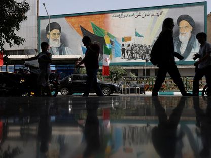 إيرانيون يسيرون بجوار لوحة جدارية عليها صورة المرشد الإيراني علي خامنئي في أحد شوارع العاصمة طهران في الساعات الأولى من دخول اتفاق وقف إطلاق النار حيز التنفيذ، طهران، إيران. 24 يونيو 2025 - REUTERS