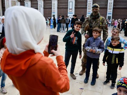 أطفال يلتقطون صورة مع مقاتل في الفصائل المسلحة بمدينة دمشق القديمة. 12 ديسمبر 2024 - Reuters