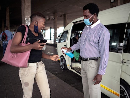 سائق سيارة أجرة يرش المعقم على يد راكبة قبل صعودها السيارة في جوهانسبورغ، جنوب إفريقيا - AFP