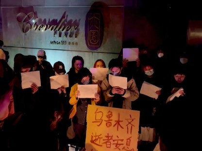 أشخاص يحملون لافتات خلال وقفة احتجاجية على ضوء الشموع أقيمت لضحايا حريق أورومتشي في شنغهاي بالصين. 26 نوفمبر 2022 - REUTERS