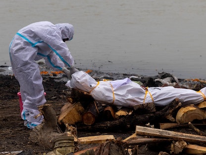  رجل يرتدي بدلة واقية بالقرب من جثة متوفي بفيروس كورونا  - REUTERS