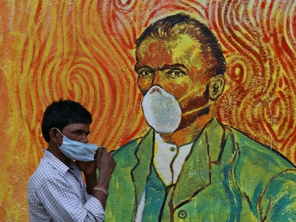 رجل يعدل قناع وجهه وهو يمشي أمام لوحة جدارية وسط انتشار فيروس كورونا في مومباي بالهند. 11 مارس 2021 - REUTERS