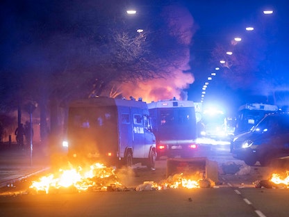 شاحنات الشرطة السويدية متوقفة بجوار صناديق قمامة محترقة وتغلق شارعاً في مدينة مالمو، 16 أبريل 2022 - AFP