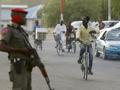 رجل يركب دراجة أمام شرطي بالقرب من اللجنة الوطنية للانتخابات في ولاية كانو بشمال نيجيريا - REUTERS