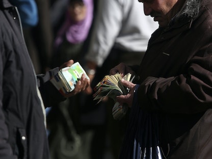 صرافون فلسطينيون يعدون النقود في أحد شوارع مدينة رام الله بالضفة الغربية. - REUTERS