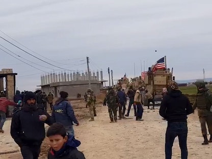 أشخاص يتجمعون بالقرب من مركبات عسكرية أميركية في قرية خربة عمو بالقرب من القامشلي. سوريا في 12 فبراير  2020. - REUTERS