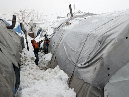 طفل يزيل الثلوج من إحدى الخيام في مخيم للنازحين بالقرب من قرية الزوف بالقرب من مدينة جسر الشغور في محافظة إدلب شمال غرب سوريا على الحدود مع تركيا- 26 يناير 2022  - AFP