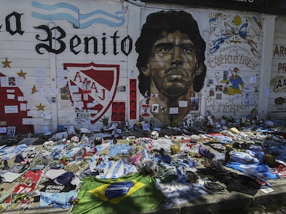 صورة الأرجنتيني دييغو مارادونا وإلى جانبها الزهور والأعلام والقمصان تكريماً للنجم الأسطوري - AFP