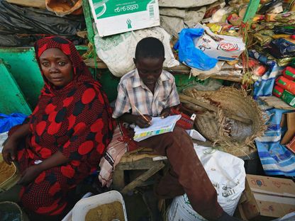 تلميذ سوداني يؤدي واجباته المدرسية بجوار والدته في سوق نيالا بدارفور، 19 سبتمبر 2017 - REUTERS