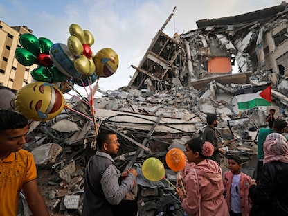 فلسطيني يبيع البالونات أمام مبنى الشروق المدمر الذي دمرته غارة جوية إسرائيلية في مدينة غزة - 21 مايو 2021  - AFP