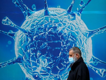 رجل يرتدي قناعاً وقائياً يمشي أمام رسم توضيحي لفيروس كورونا في أولدهام ببريطانيا. 3 أغسطس 2020 - REUTERS