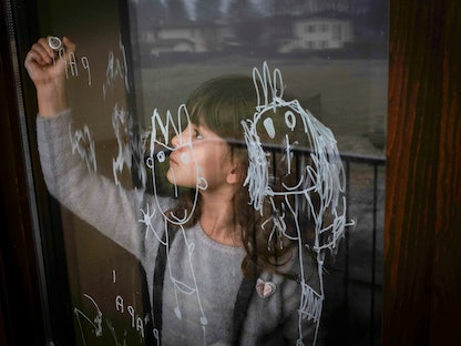 طفلة ترسم على نافذة غرفة نومها في منزلها بإقليم لومبارديا شمال إيطاليا، خلال فترة الإغلاق العام - ديسمبر 2020. - REUTERS