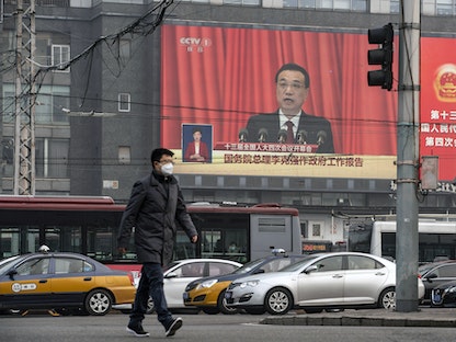 أحد شوارع العاصمة الصينية بكين ويظهر في الخلفية شاشة تعرض جلسة المجلس الوطني لنواب الشعب الصيني - Bloomberg