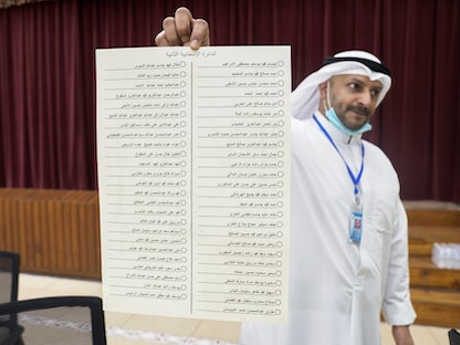 مسؤول كويتي يرفع قائمة بأسماء مرشحي الدائرة الثانية في انتخابات مجلس الأمة داخل أحد مراكز الاقتراع- 5 ديسمبر 2020 - REUTERS