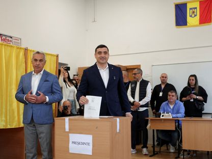 المرشح الرئاسي جورج سيميون يدلي بصوته بينما يقف إلى جانبه كالين جورجيسكو في مركز اقتراع خلال الجولة الأولى من انتخابات رومانيا. 4 مايو 2025 - Reuters