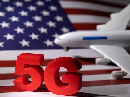 مجسم لطائرة إلى جانب شعار تقنية "5G" أمام العلم الأميركي - REUTERS