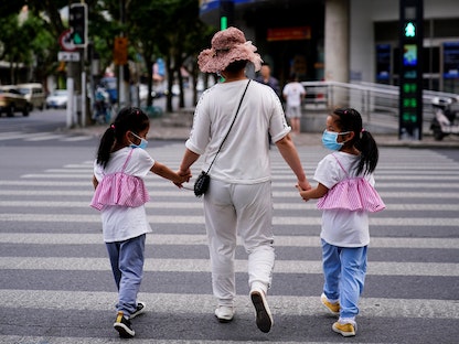 سيدة تقطع الشارع مع ابنتيها التوأمين في أحد أحياء شنغهاي- 7 يونيو 2021 - REUTERS