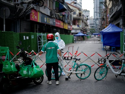 عامل يرتدي بدلة واقية يحصل على طعام من عامل توصيل في منطقة سكنية مغلقة وسط تفشي فيروس كورونا في شنغهاي بالصين - 25 مايو 2022 - REUTERS