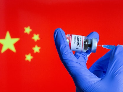 زجاجة صغيرة عليها ملصق "لقاح فيروس كورونا" خلف العلم الصيني - 30 أكتوبر 2020 - REUTERS