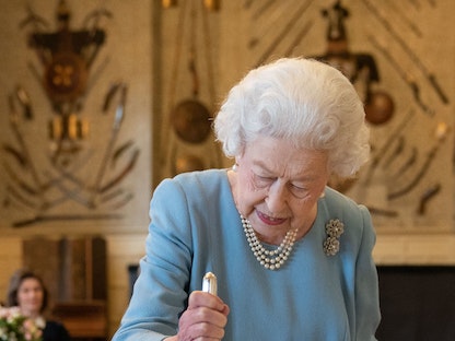 ملكة بريطانيا إليزابيث الثانية تقطع كعكة للاحتفال ببداية اليوبيل البلاتيني خلال حفل استقبال في مقر إقامة الملكة في نورفولك - 5 فبراير 2022. - AFP