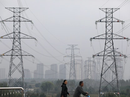 أشخاص يمشون أمام أبراج الكهرباء في شنيانغ، مقاطعة لياونينغ، الصين. 29 سبتمبر 2021. - REUTERS