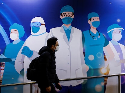 رجل يرتدي قناعاً للوجه يمر بجوار إعلان لدعم المهنيين الطبيين بعد تفشي مرض فيروس كورونا، في هونج كونج، الصين - 24 فبراير 2022 - REUTERS