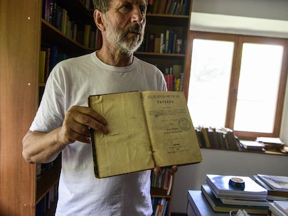 ستيفو ستيبانوفسكي يمسك أحد المجلدات في مكتبة قرية بابينو غرب مقدونيا الشمالية - 11 يوليو 2022 - AFP