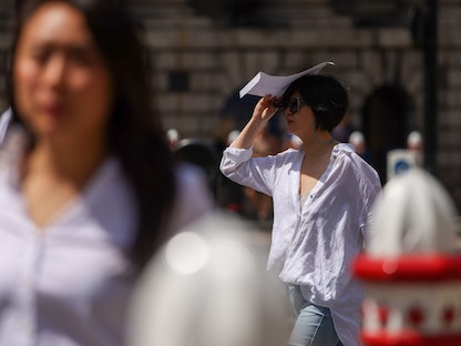 امرأة تستخدم مظروفاً لحماية نفسها من أشعة الشمس في لندن بريطانيا - 17 يونيو 2022 - Bloomberg