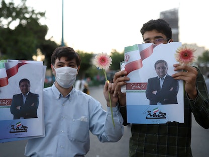 مناصران للمرشح الرئاسي عبد الناصر همتي يحملان ملصقات دعائية له في أحد شوارع طهران - 16 يونيو 2021 - REUTERS
