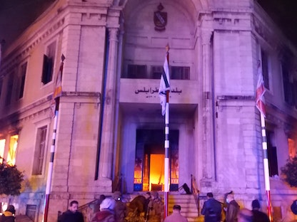 أشخاص أمام بلدية طرابلس شمال لبنان بينما تندلع الحرائق داخلها جراء مواجهات بين محتجين وقوى الأمن- 28 يناير 2021 - REUTERS