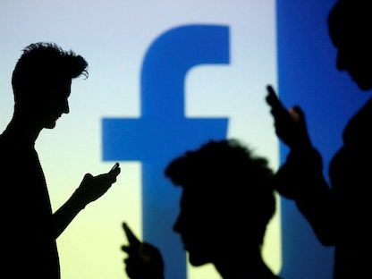 أشخاص يحملون هواتفهم الذكية أمام شعار "فيسبوك" - REUTERS