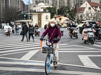 امرأة تعبر شارعاً على دراجة في منطقة جينجان بمدينة شنغهاي الصينية. 22 فبراير 2023 - AFP
