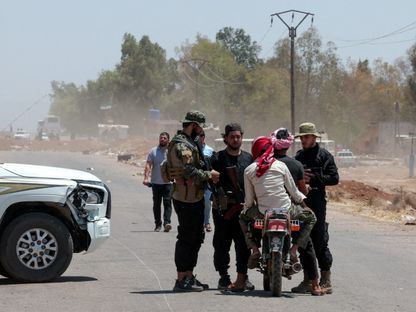 أفراد من قوات الأمن السورية يتحدثون مع بدو على دراجة نارية عند نقطة تفتيش بالقرب من مدينة السويداء، سوريا. 24 يوليو 2025 - Reuters